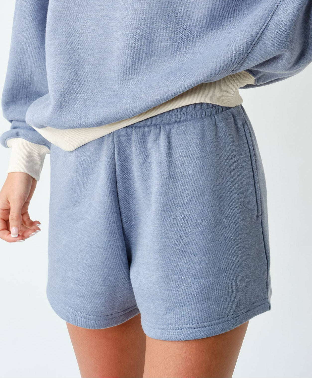 Woman wearing a light blue sweatshirt and shorts set with a matching cap on a white background