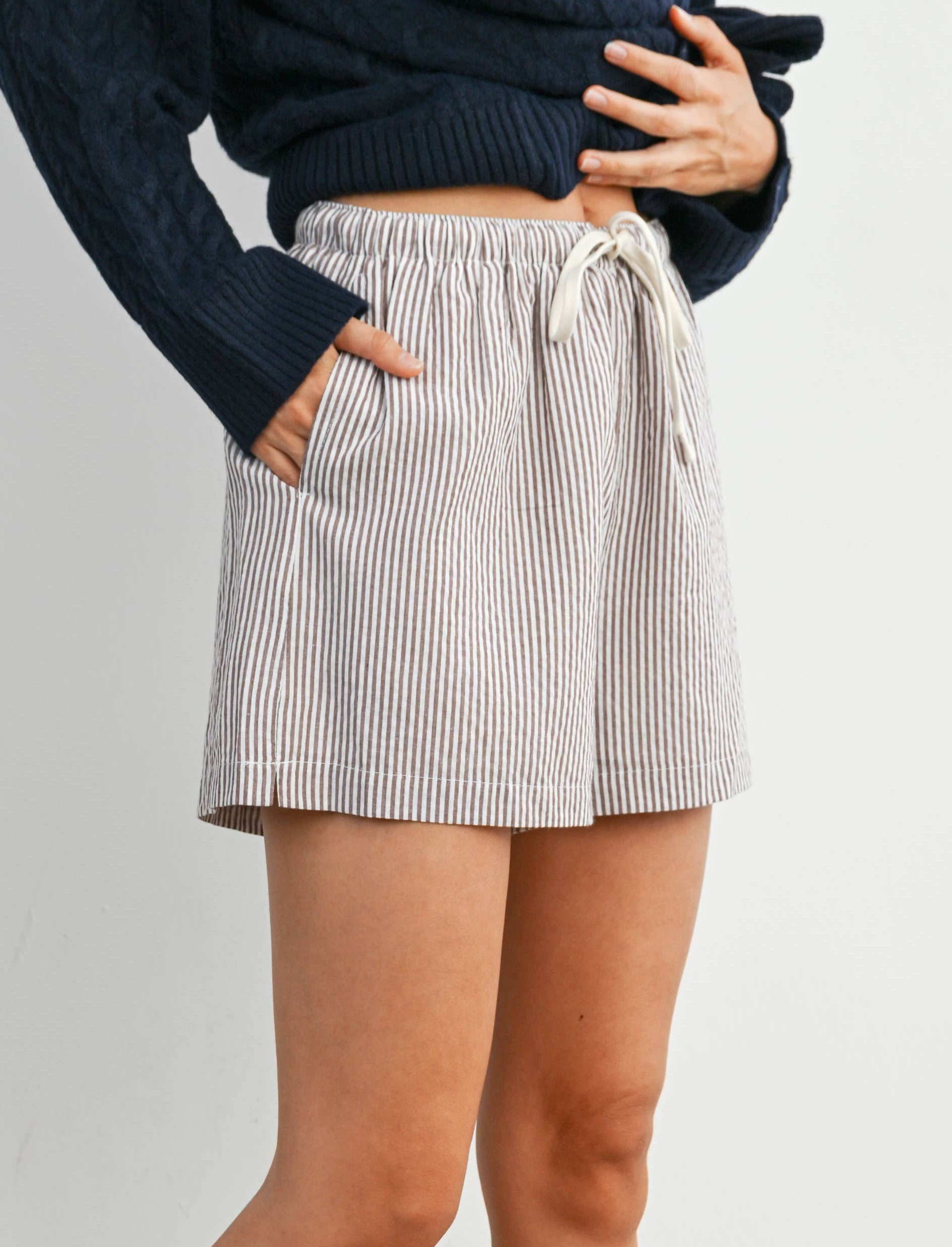 Person wearing a striped skirt, navy sweater, white socks, and brown shoes on a plain background