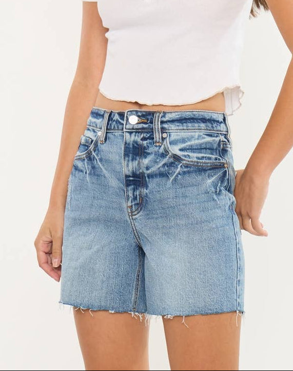Woman wearing a white short-sleeve top and blue denim shorts on a plain background