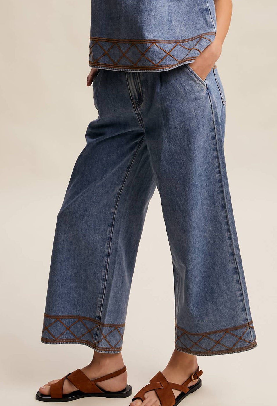 Woman wearing a denim sleeveless top and wide-leg pants on a beige background